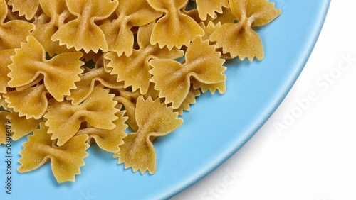 Uncooked wholegrain farfalle pasta on a round blue dish over a white background
