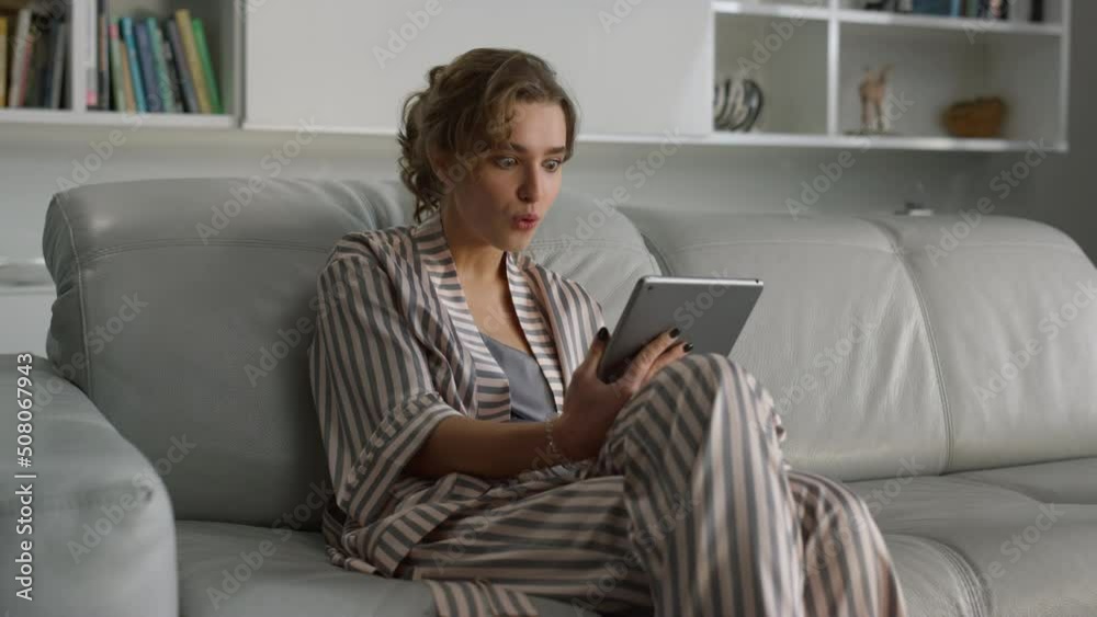 Surprised girl checking bank account on digital tablet computer in living room Surprised girl checking bank account on digital tablet computer in living room