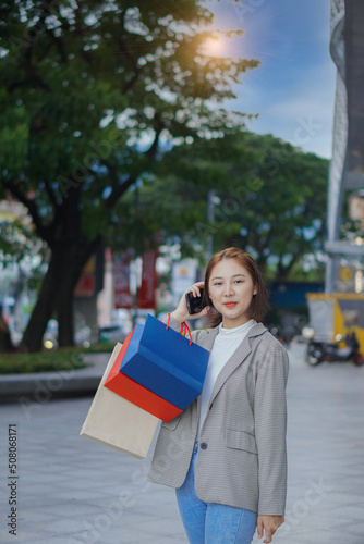 Happy Asian woman standing in front of a shopping mall at a shopping center. . Asian woman holding shopping bags, woman concept shopping stand and vertically holding multicolored paper bags.