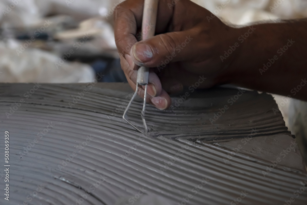 Obraz premium Close up of male sculptor holding tool and making art on clay. Clay master moulding. Clay modelling.