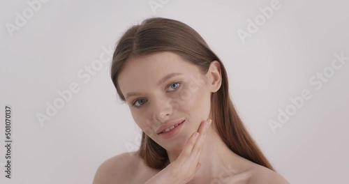 Beautiful female face. Portrait of tender young woman with clean fresh skin touching own face over grey background. Concept of people, wellness and natural beauty.