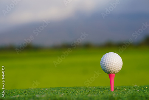 Golf ball on tee in beautiful golf course at sunset background.