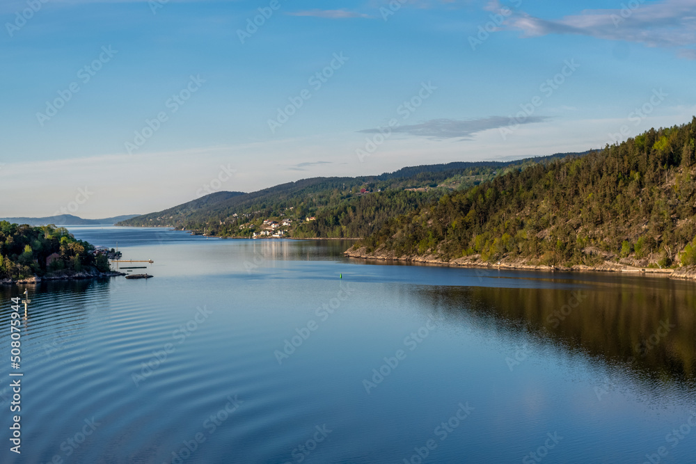 stilles glattes Wasser des Fjords im Vordergrund mit hügelig bewaldeter Landschaft im Hintergrund