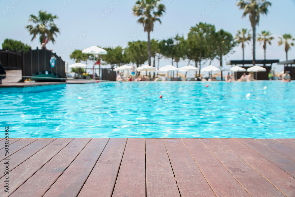  Wooden deck in front with blurred background of swimming pool in hotel