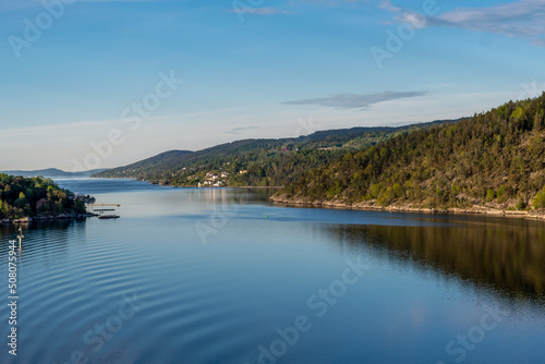 stilles glattes Wasser des Fjords im Vordergrund mit hügelig bewaldeter Landschaft im Hintergrund