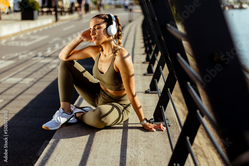 Fotografiet Pretty young woman with earphones takes a break after running in urban area