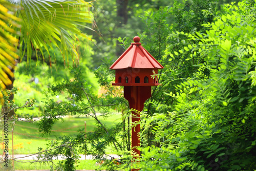 Cute red birdhouse in the beautiful park. Beautiful spring or summer day. Selective focus.