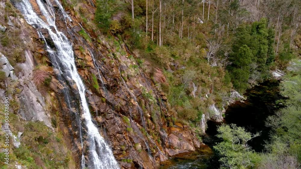 waterfall on the Sor River by the rocky cliff surrounded by forests with freshwater fishing area. Drone shot, traveling forward, rolling to the right.Mirador Aguas Caidas, Manón, Lugo, Galicia waterfall on the Sor River by the rocky cliff surrounded by forests with freshwater fishing area. Drone shot, traveling forward, rolling to the right.Mirador Aguas Caidas, Manón, Lugo, Galicia