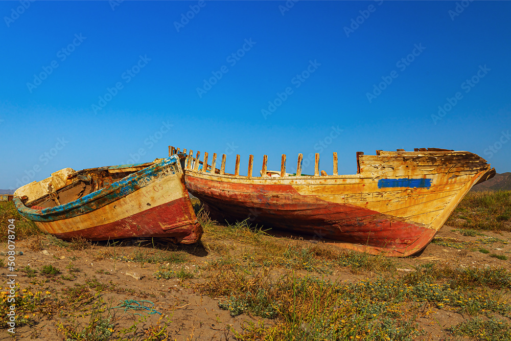the wrecks of boats on the sandy shore next to the sea