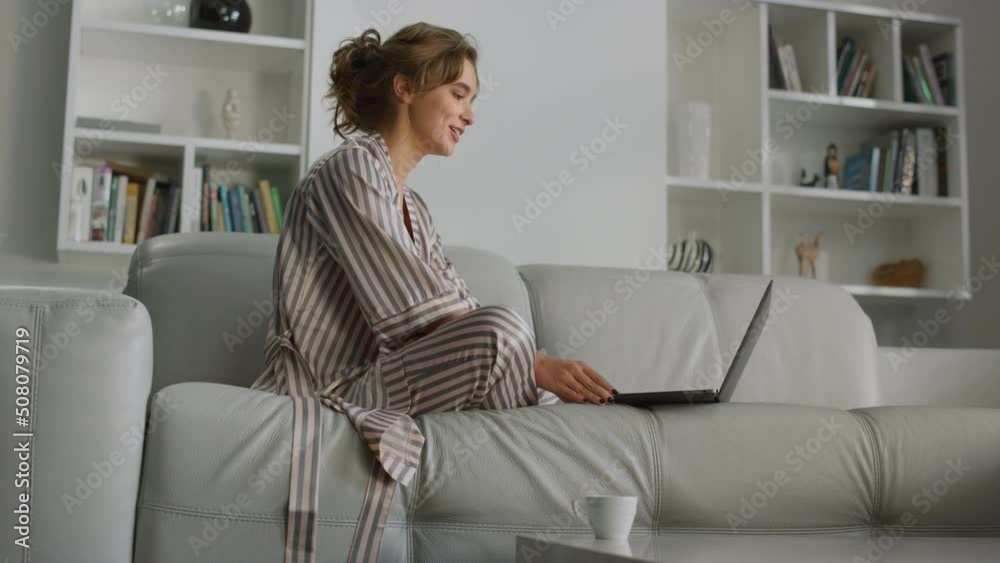 Girl making video call on living room couch. Happy woman waving hand at laptop Girl making video call on living room couch. Happy woman waving hand at laptop