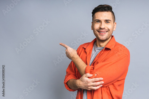 Look over there! Happy young handsome man in casual pointing away at copyspace and smiling while standing isolated over white grey background.