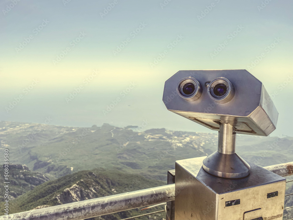 binoculars on an observation deck made of gray metal. sightseeing tour, observing the view from the mountains. binoculars against the backdrop of a mountainous plain with greenery