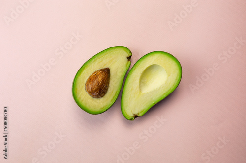 Two halves of an avocado lying side by side on a pink background top view. Fresh fruit cut in half flatley photography.