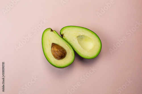 Two halves of an avocado lying side by side on a pink background top view. Fresh fruit cut in half flatley photography.