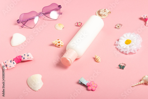 Children's sunscreen, sunglasses accessories and jewelry on a pink background. Cosmetics and accessories for little girls, flat lay. Summer baby cosmetics