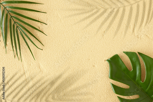Summer day scene with green tropical leaves and shadows on sand background. Flat lay. Minimal summer exotic concept with copy space.