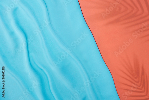 Creative flat lay with blue silk fabric and tropical leaves shadows on pastel pink background. Minimal summer concept.