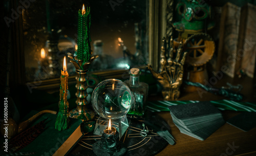 Illustration of magical stuff....candle light, Chrystal ball, magic wand, book of spells dark background, Slytherin school, green aesthetic, Halloween time © T.Den_Team