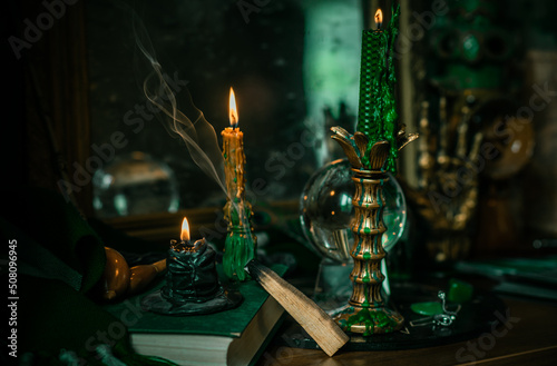 Illustration of magical stuff....candle light, Chrystal ball, magic wand, book of spells dark background, Slytherin school, green aesthetic, Halloween time photo