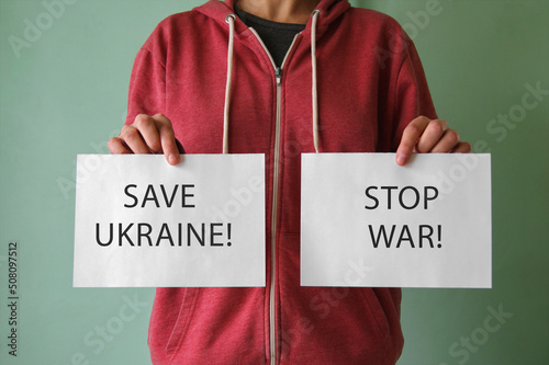 A young man holds a sheet with the inscription SAVE UKRAINE and STOP WAR.