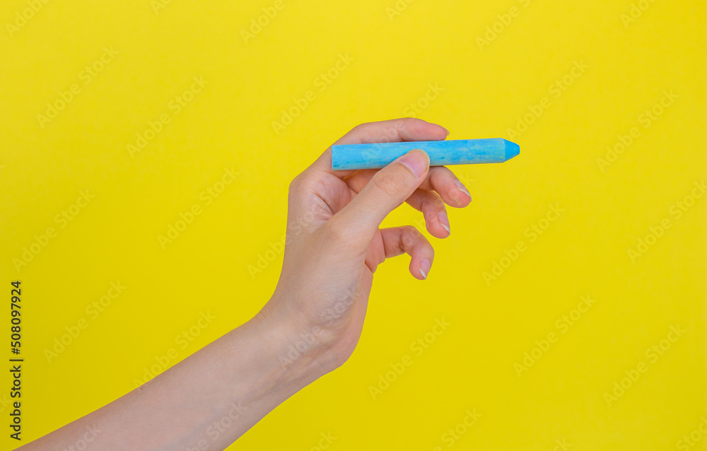 Fototapeta premium Hand holding blue chalk isolated on yellow background.