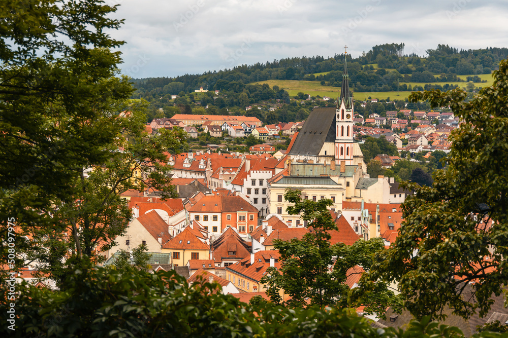 The view of St. Vitus church and the town of Cesky Krumlov from the castle courtyard framed by trees. Český Krumlov, South Bohemia, Czech Republic.