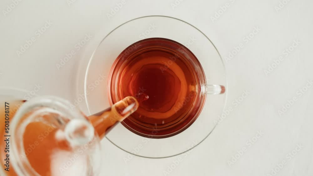 Pouring black tea in cup top view. Fresh hot herbal tea, healthy morning, detox drink on white background.
