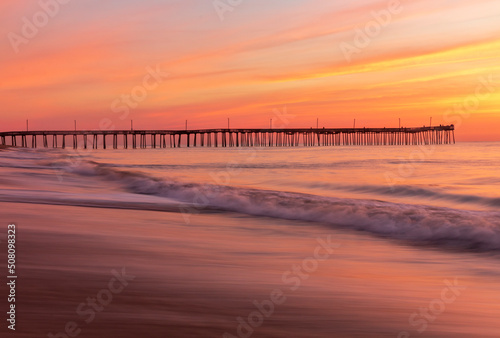 dramatic pastel colors of the summer morning sky as the waves of the Atlantic waters rush in the shores and pier of Virginia Beach.