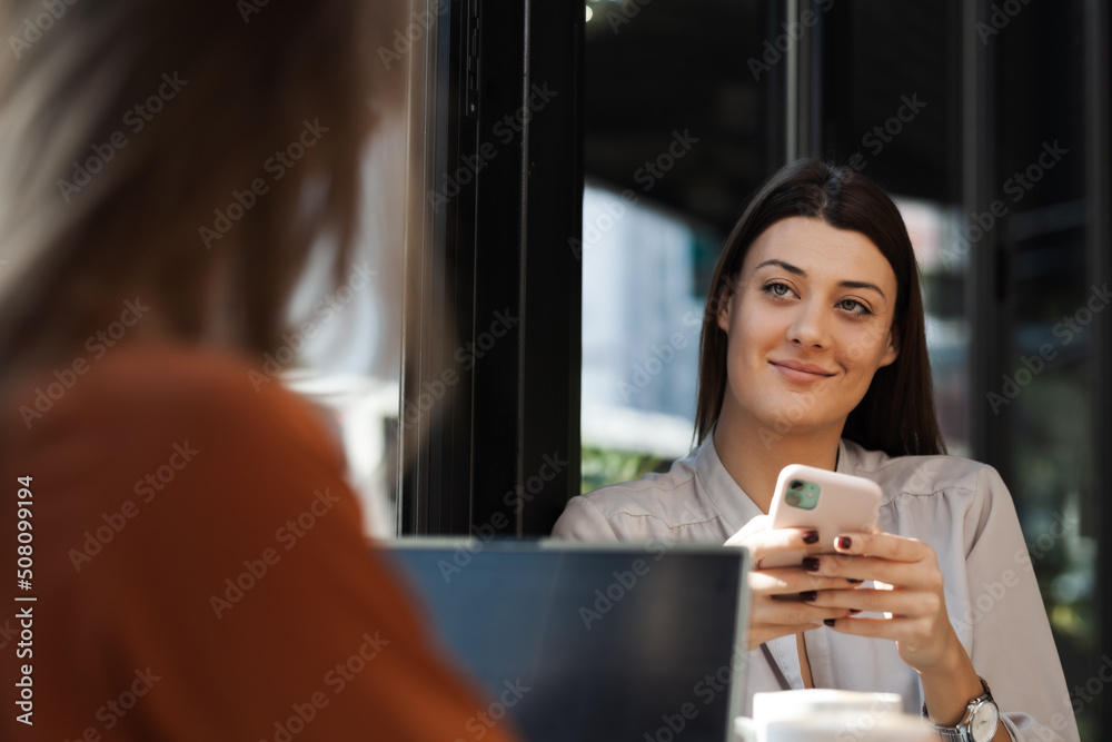 Two young business women in a cafe having one on one meeting. Friends after work talking gossiping and having coffee at a window table on a sunny day.. Two young business women in a cafe having one on one meeting. Friends after work talking gossiping and having coffee at a window table on a sunny day..