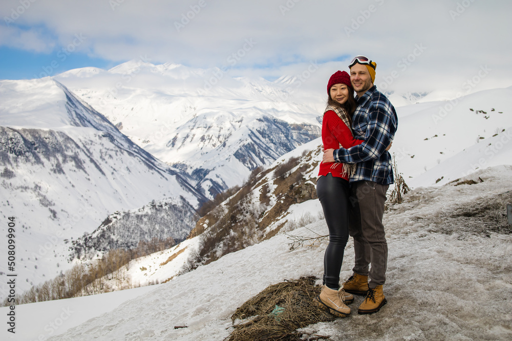 A loving couple plays together in the snow outdoors. Winter holidays in the mountains. Man and woman in knitted clothes have fun on weekends.