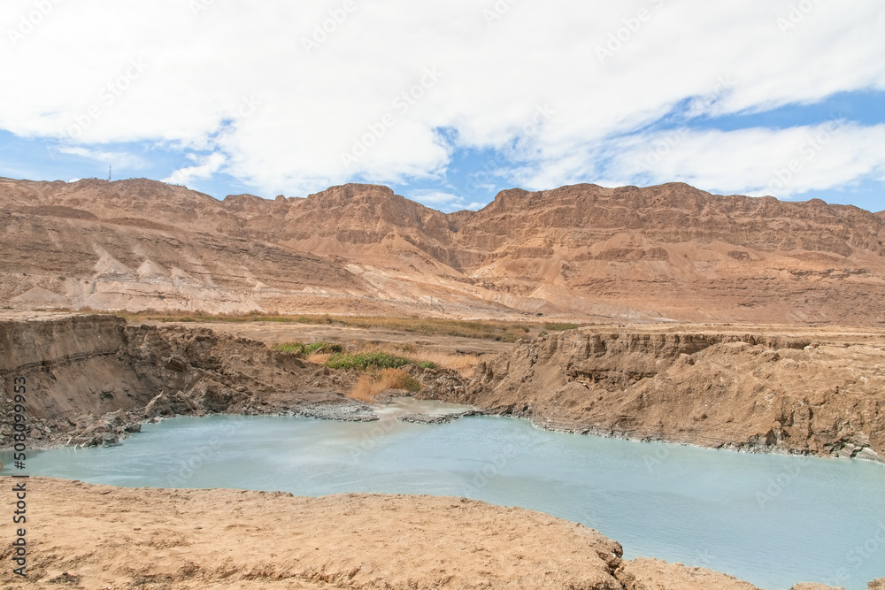 Sinkhole filled with turquoise water, near Dead Sea coastline. Hole formed when underground salt is dissolved by freshwater intrusion, due to continuing sea-level drop. . High quality photo