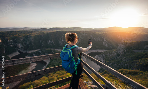 Young woman hiker taking photo of canyon with smart phone from canyon viewpoint