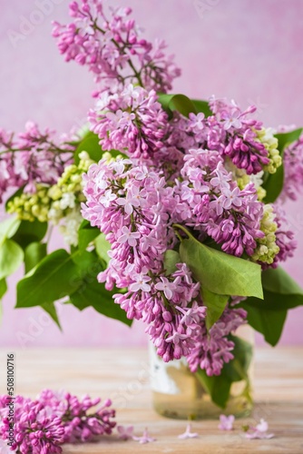 Branches of pink and white lilacs in a glass jar on a pink concrete background. Lilac blossom. Greeting cards with a composition