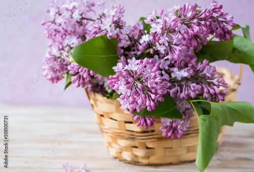 Branches of pink and white lilacs in a wicker basket on a pink concrete background. Lilac blossom. Greeting cards with a composition for the holiday, covers for notebooks