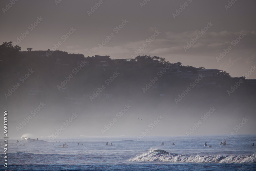 Surfers in the Ocean with morning mist and mountain view in background Surfers in the Ocean with morning mist and mountain view in background