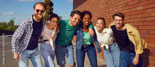 Happy diverse friends enjoying time together. Six different young Caucasian, Afro American and Asian people in fashion clothes standing on street, hugging each other, looking at camera and smiling © Studio Romantic