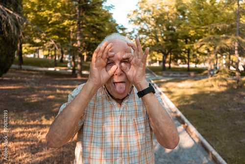 Hombre mayor con gesto divertido y con la lengua fuera, en el parque. Fotografía horizontal. photo