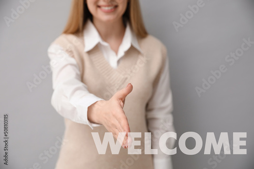Closeup view of happy young woman offering handshake on grey background, focus on hand. Welcome to team