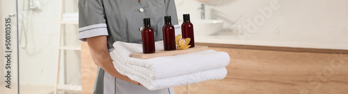 Chambermaid holding fresh towels with flower and shampoo bottles in hotel bathroom  closeup. Banner design
