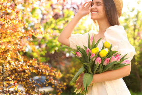 Beautiful young woman with bouquet of tulips in park, focus on flowers. Space for text