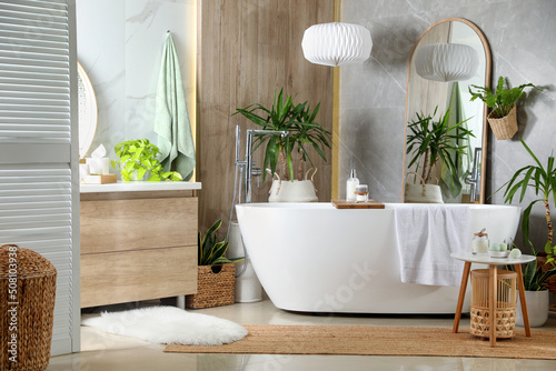 Modern white tub and beautiful green houseplants in bathroom. Interior design