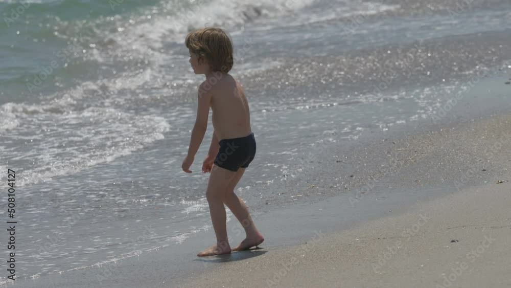 Little child walk to seaside waves, boy feeling soft sand Little child walk to seaside waves, boy feeling soft sand