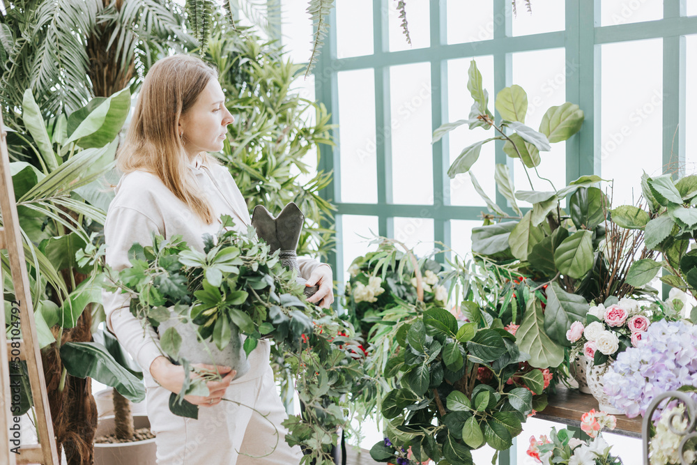young woman waters flowers from watering can in greenhouse with tropical plants and potted plants, spring concept of urban and home jungles, place for rest and relaxation mental health young woman waters flowers from watering can in greenhouse with tropical plants and potted plants, spring concept of urban and home jungles, place for rest and relaxation mental health
