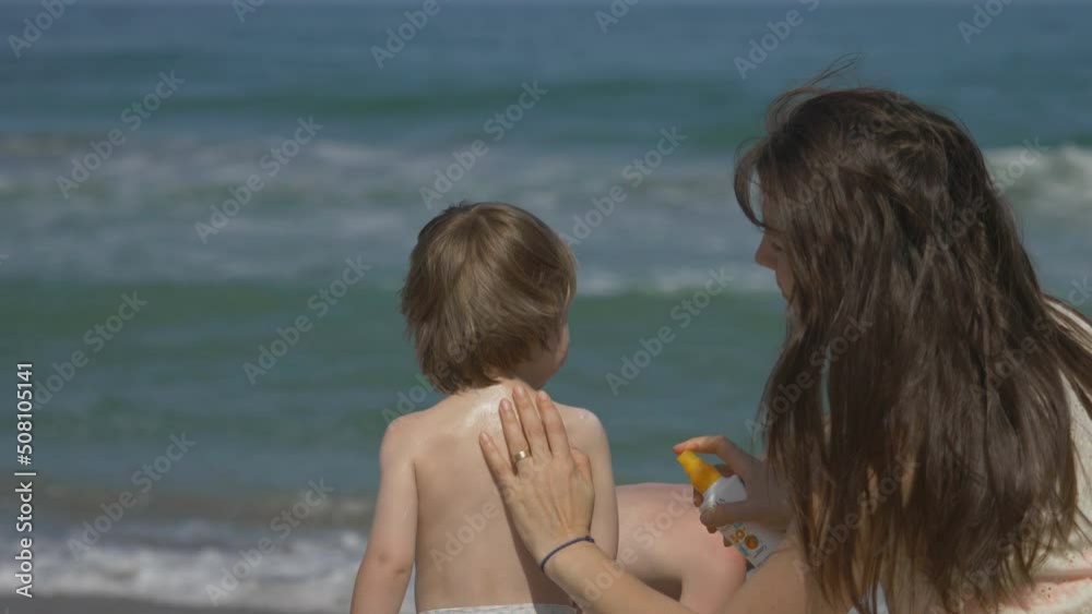 Mother applying sun cream protection to baby child back, blue sea waves, parent love Mother applying sun cream protection to baby child back, blue sea waves, parent love