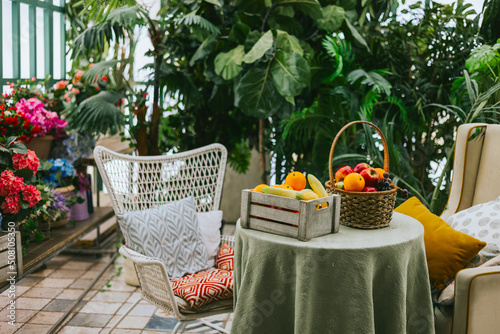 cozy veranda, table with basket of fruits and an armchair, greenhouse or a terrace for rest and relaxation, blooming garden