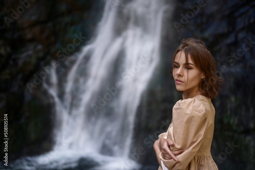 Pretty young girl with brown hair against the backdrop of waterfall.