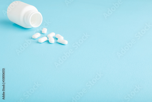 White pills and plastic bottle on light blue table background. Pastel color. Closeup. Empty place for text or logo.