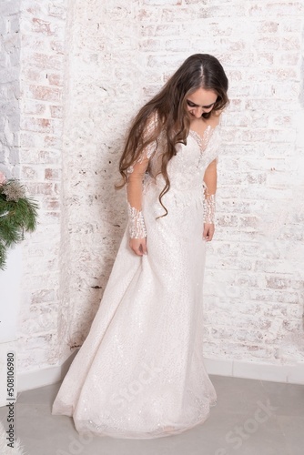 The bride in full growth, against the backdrop of a white brick wall.