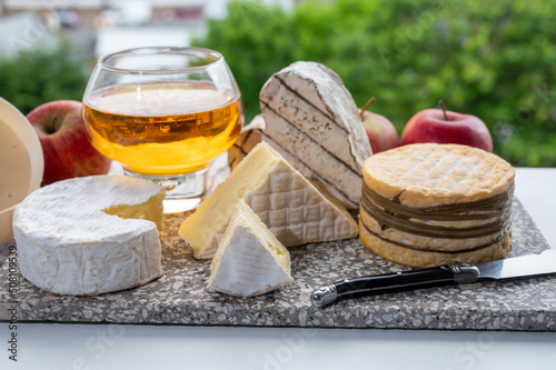 Cow cheeses of Normandy - camembert, livarot, neufchatel, pont l'eveque and glass of apple cider drink with houses of Etretat village on background, Normandy, France photo