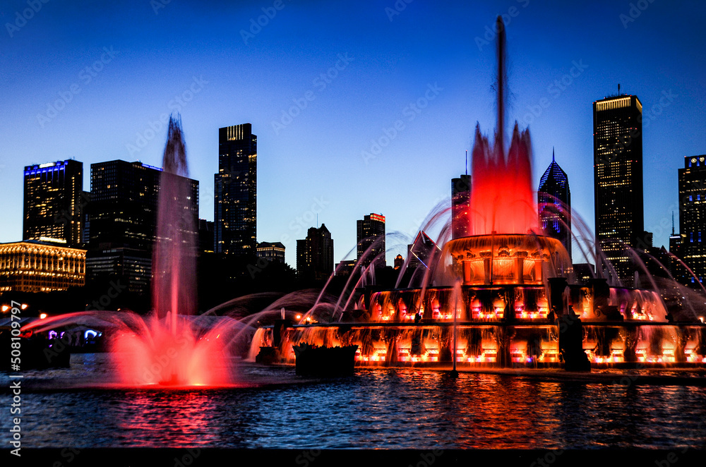 Buckingham Water fountain in red as the twilight sky turns purple silhouetting the Chicago city skyline.